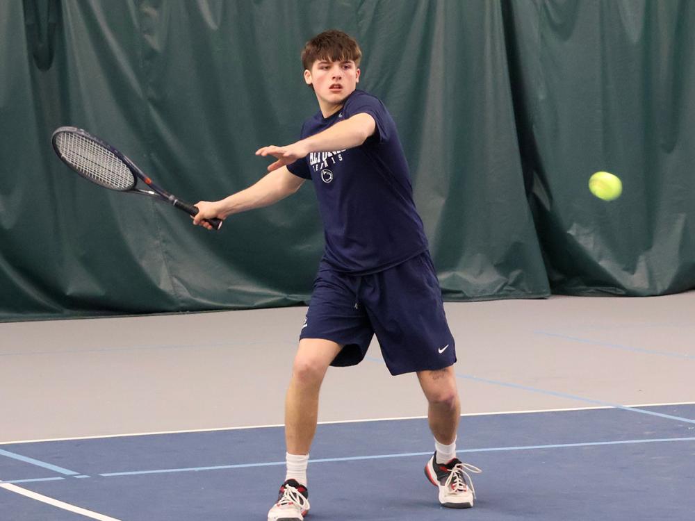 Jackson Newell prepares to return a tennis shot on an indoor court, focused on the approaching ball with racket extended.