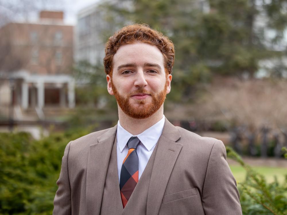 Emmanuel Kraft stands outside in a brown suit.