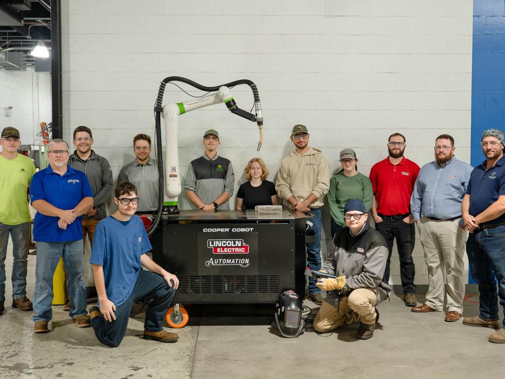 A group of about a dozen students gather round an industrial robot