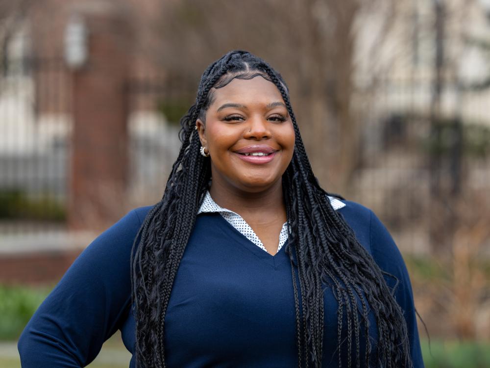 Trinidy Manison stands outdoors wearing a blue sweater and collared white shirt underneath.