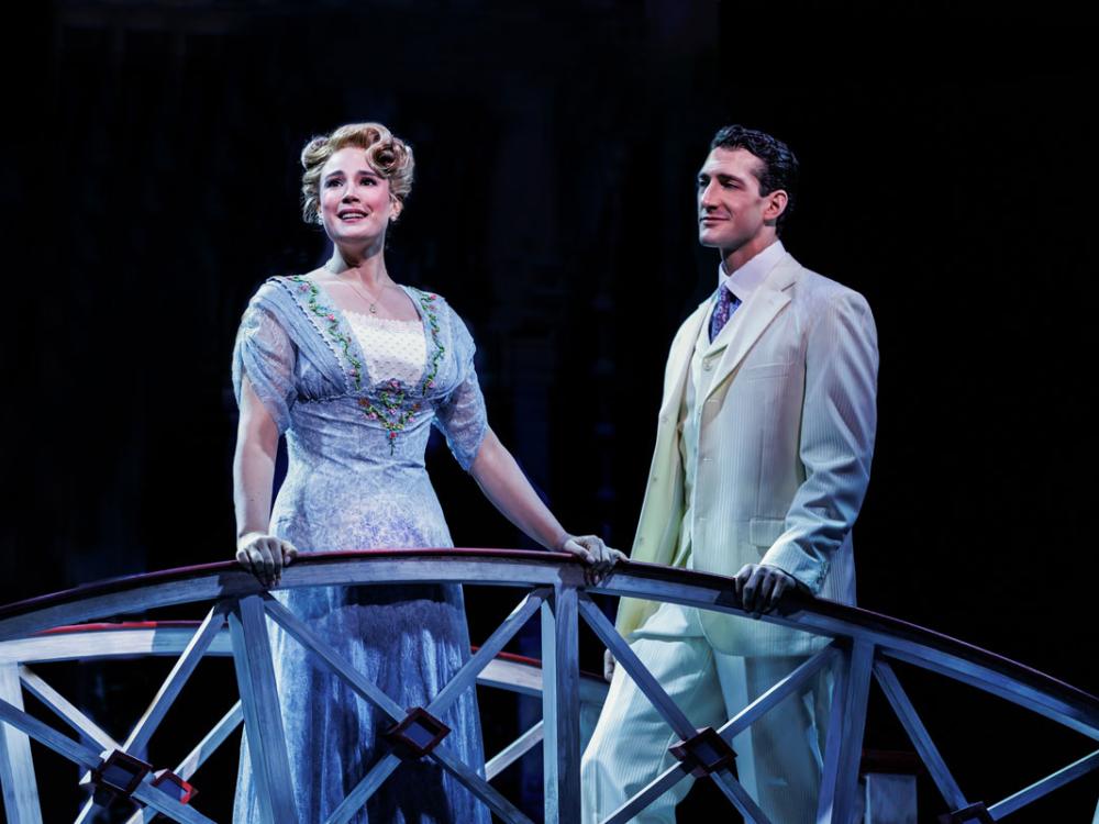 A man stands at a fence and sings while a man looks on.