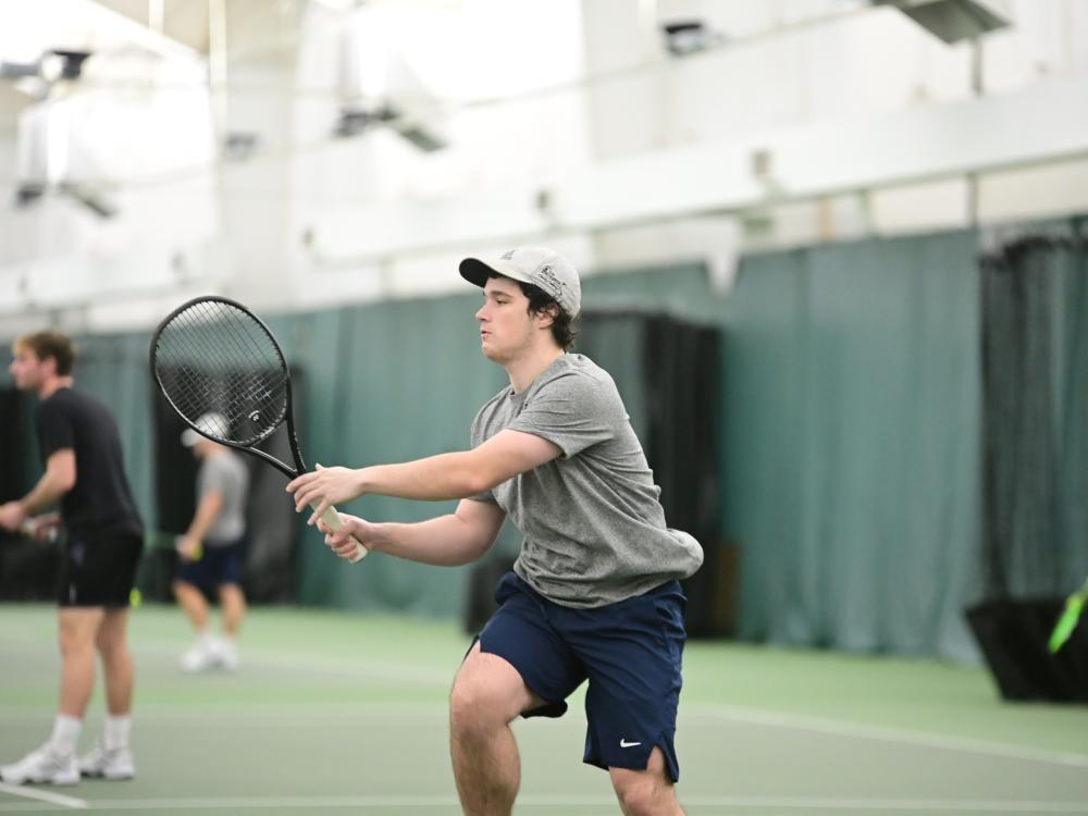 A member of the Penn State Behrend men's tennis team hits the ball during an indoor match.