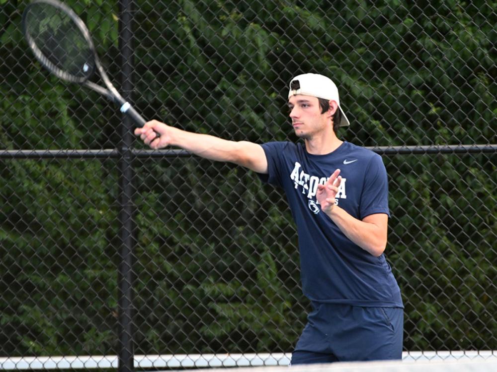 Penn State Altoona tennis player Nick Beard reaches out for a forehand shot during a match, focused and in motion on the court.