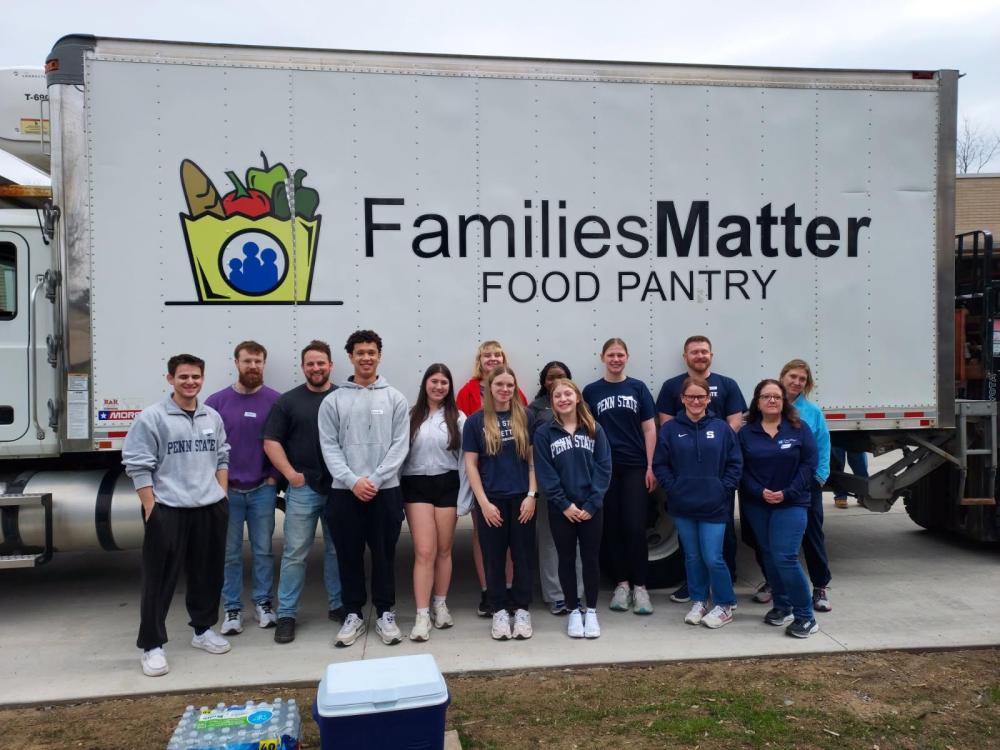 Students standing outside in front of a box truck with the words Families Matter Food Pantry printed on the side of it.
