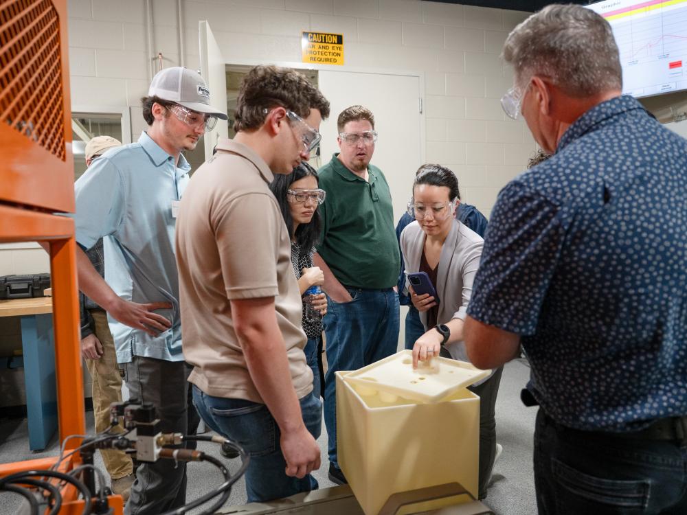 Several people gather around a polymer molding project in a room