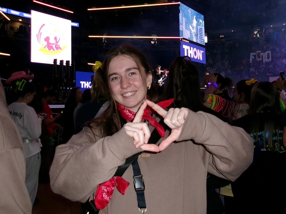Olivia Steinmetz stands on the floor of the Bryce Jordan Center during THON forming a diamond with her thumbs and forefingers.