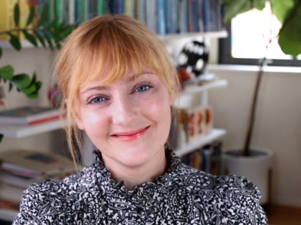 headshot photo of Kelli Anderson smiling at camera, with blond hair pulled back and wearing a black knit sweater