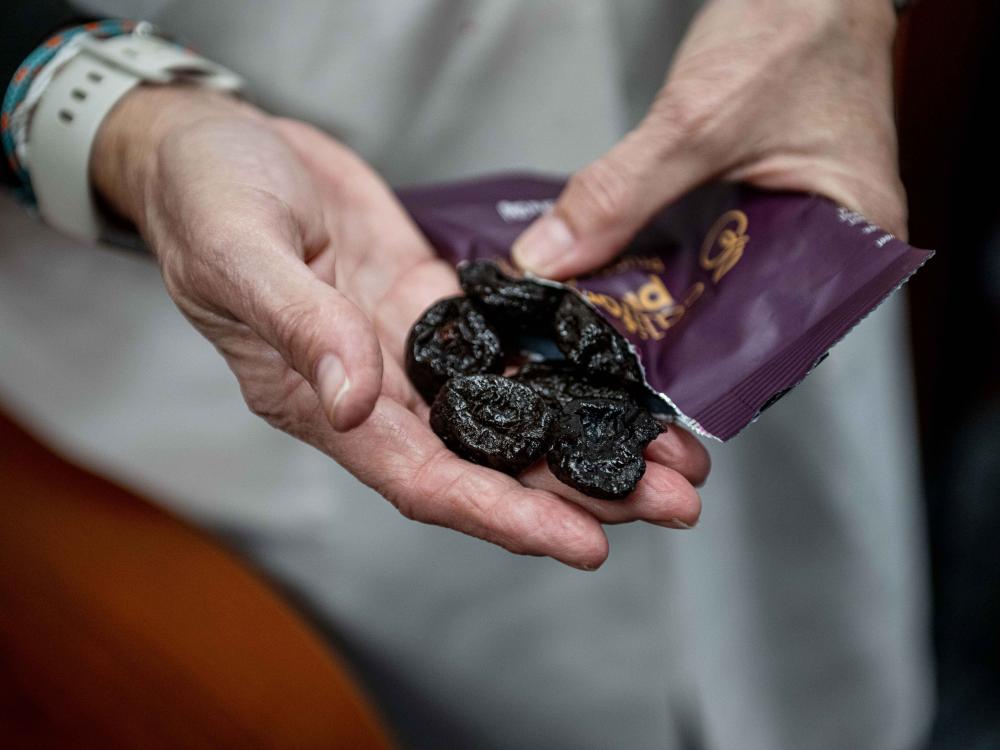 An older woman's hand with six prunes in her palm