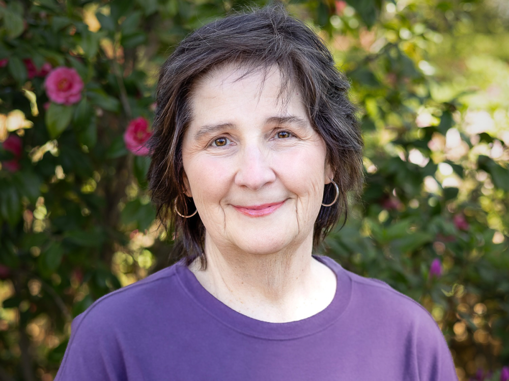 Candice Yekel in a purple shirt, standing in front of garden scenery.