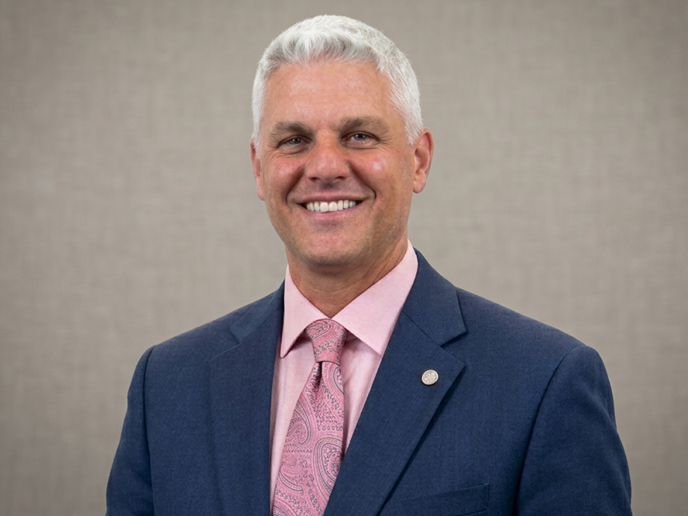 Wes Moschetto smiling in a business suit and tie.