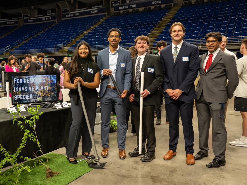 Engineering students pose next to their capstone design project for the removal of invasive plant species.