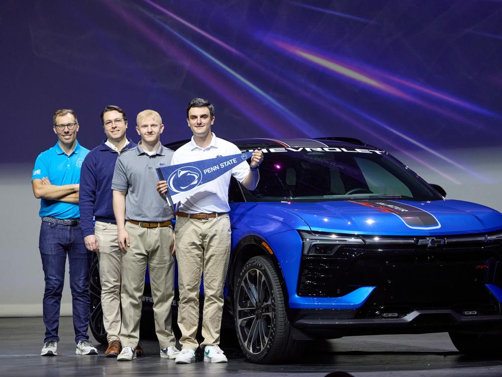 Members of the Penn State Advanced Vehicle Team stand on stage holding a Penn State pennant flag, in front of a Chevrolet Blazer Super Sport. 