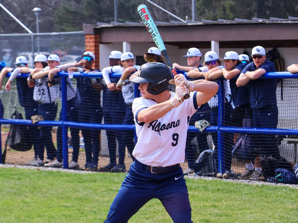 Zach Ingold at bat in front of teammates leaning on a dugout fence during a game.
