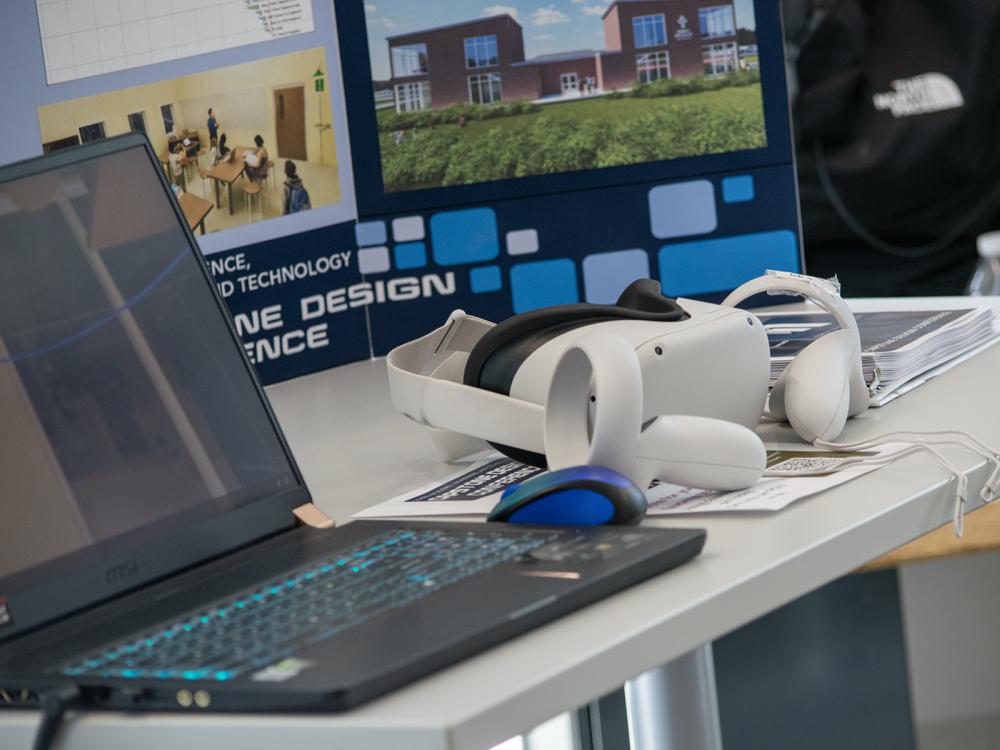 A laptop and VR headset are on display near a poster about the Capstone Design Conferenceeeeeeeeee