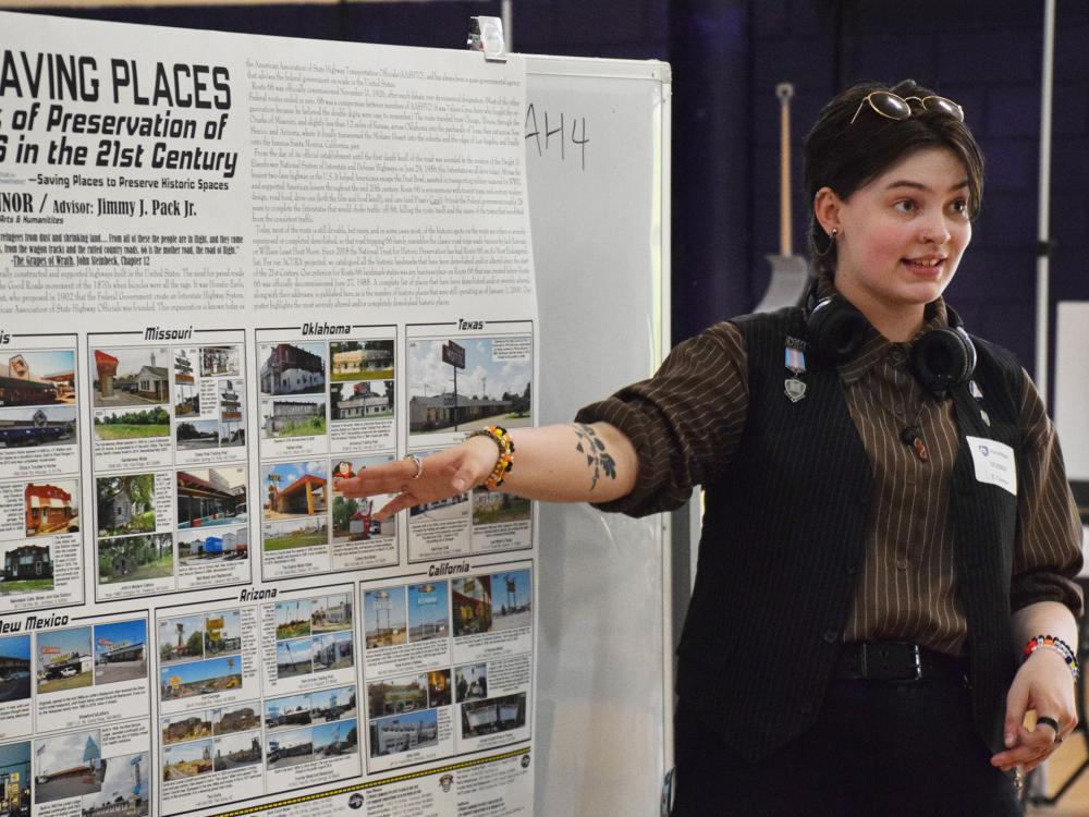 student presenting research and pointing at a poster