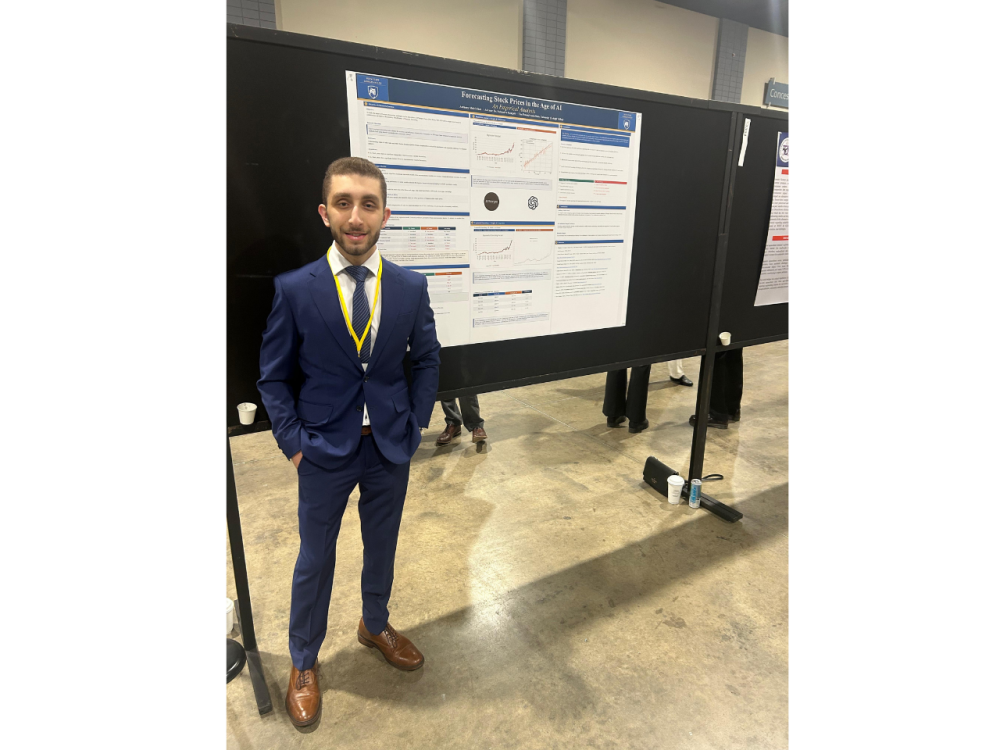 A student stands next to a research poster at a conference.