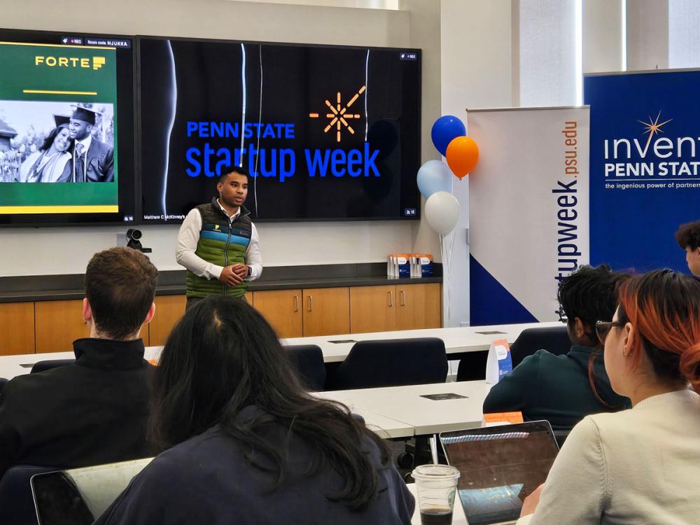 Asher Carr presents to a seated audience during Penn State Startup Week, standing in front of a large screen displaying the event title.