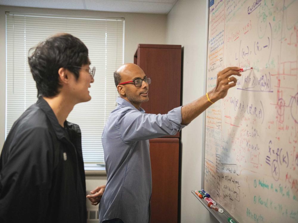 Bharath Sriperumbudur writes on white board while student looks on