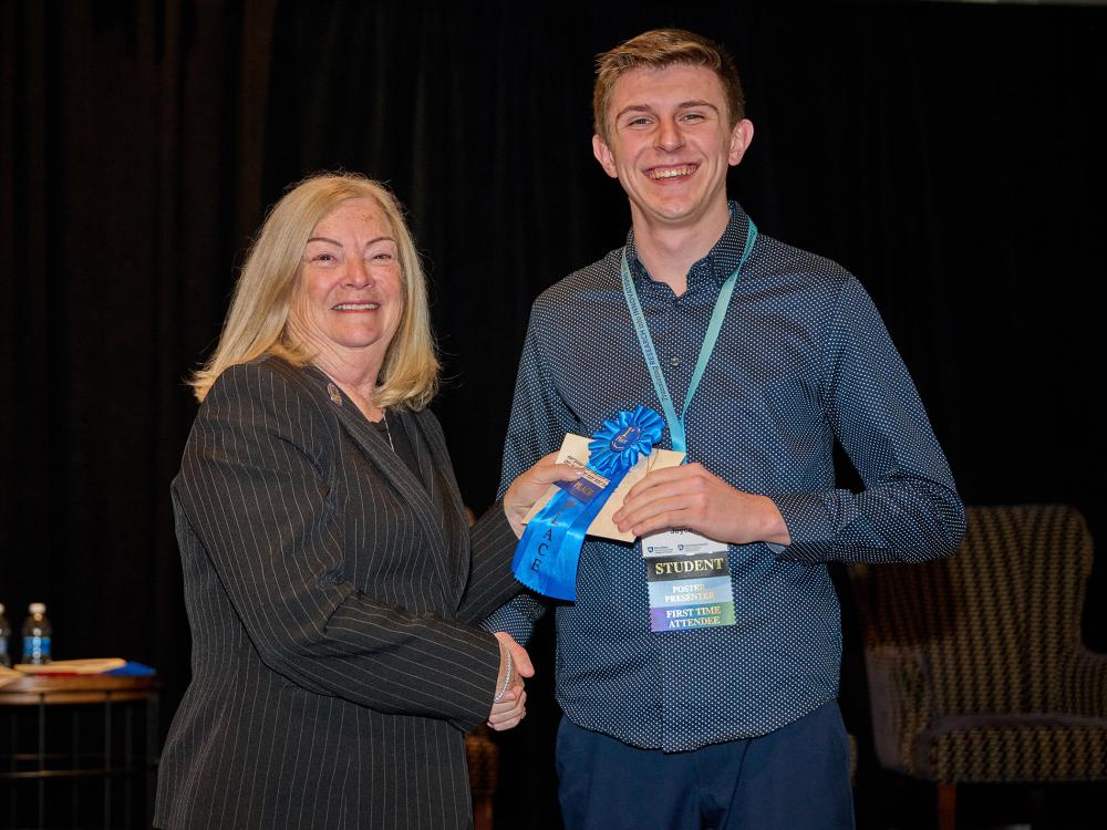 A smiling person gives another smiling person an award at a ceremony