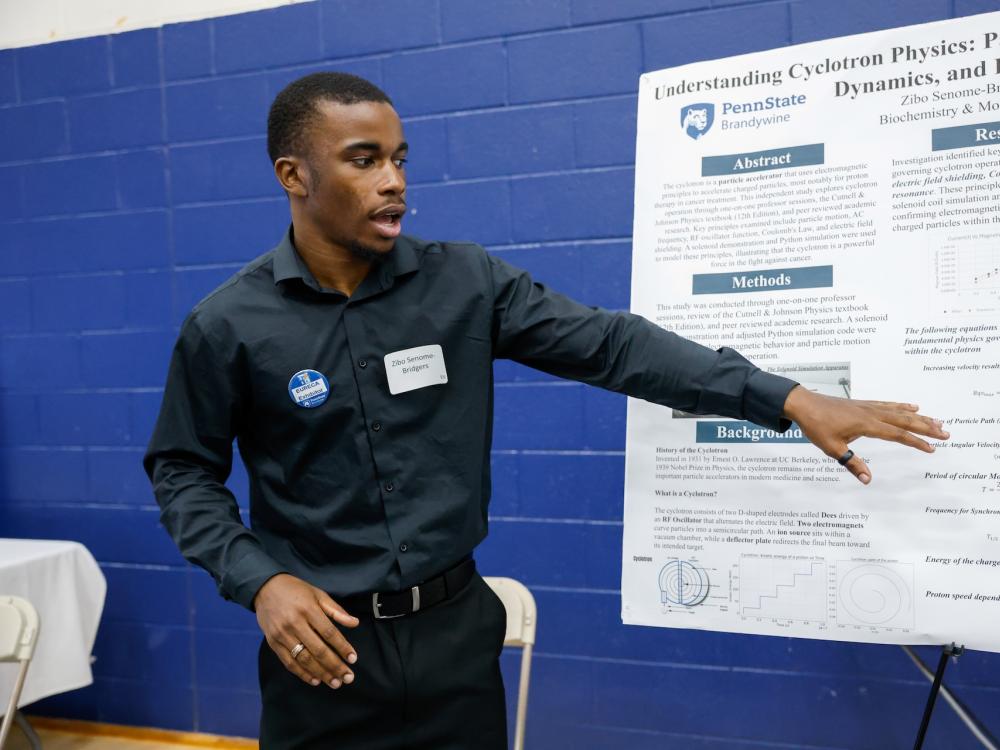 student talking about his work while gesturing to a poster he made about proton radiation