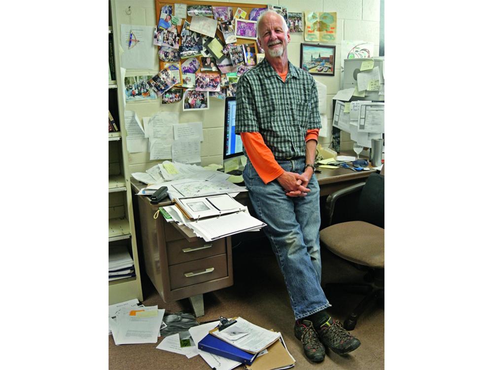 Chris Uhl in his office, leaning on his desk surrounded by papers, books and photos tacked to the wall.
