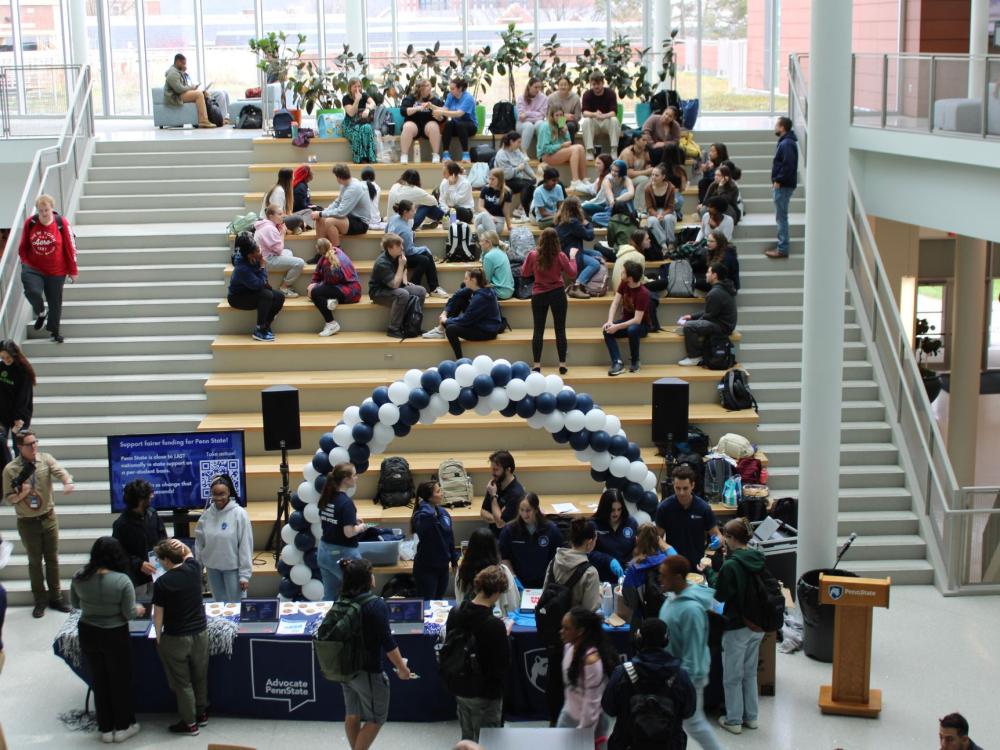 Students gather in a campus atrium around an advocacy table with a balloon arch.