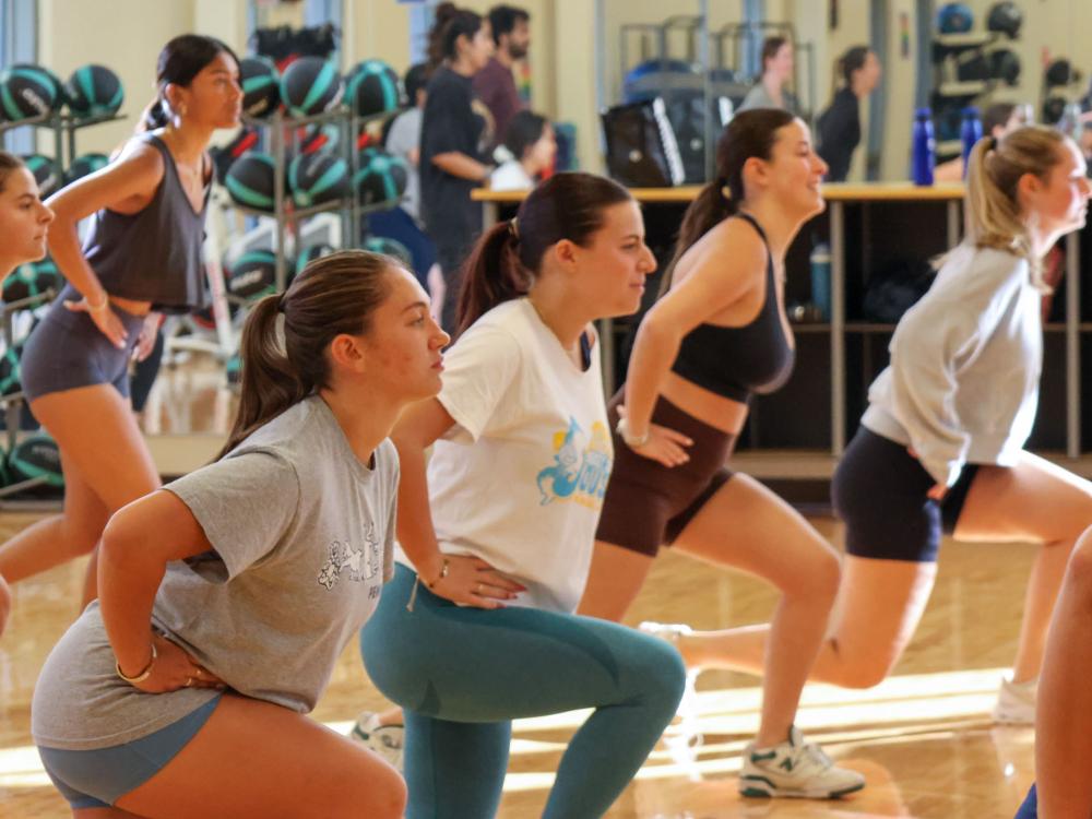 Class participants stretch in a gym during warmup