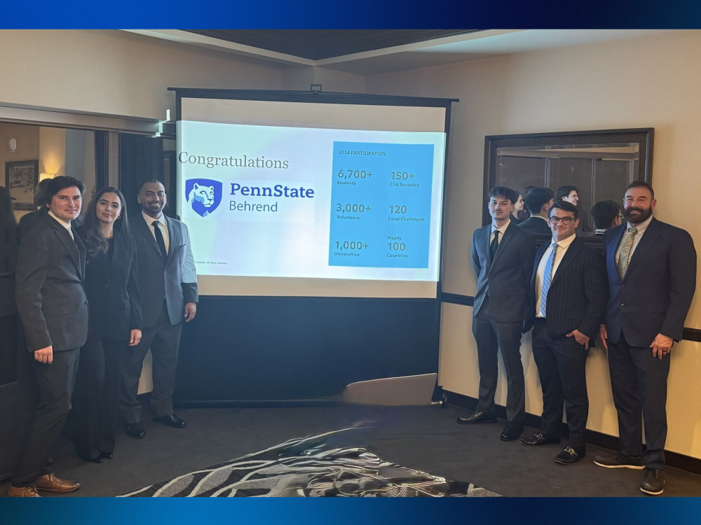 Six people wearing business attire stand in a conference room in front of a screen with the Penn State Behrend logo.