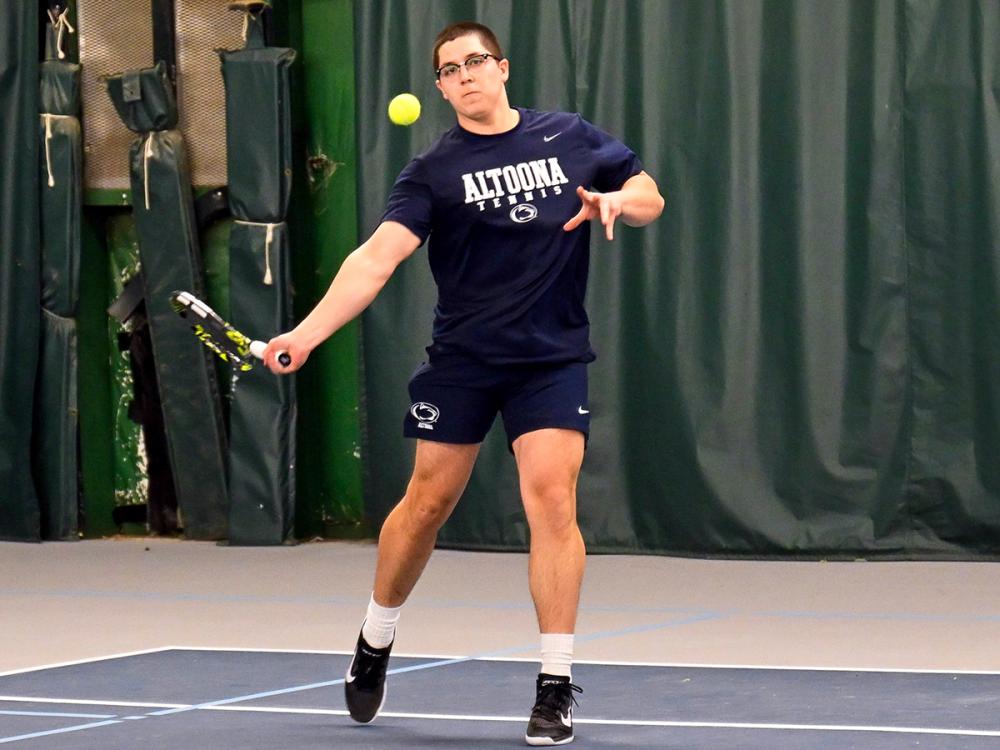 Gabriel Lopez, wearing an Altoona Tennis shirt and shorts, hits a forehand during an indoor match, with the tennis ball midair in front of him.