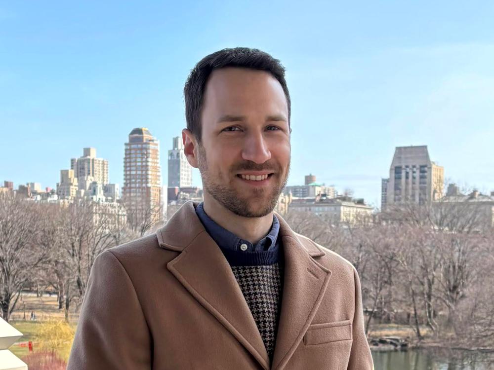 person with short dark hair and beard in woold coat with city skyline in background