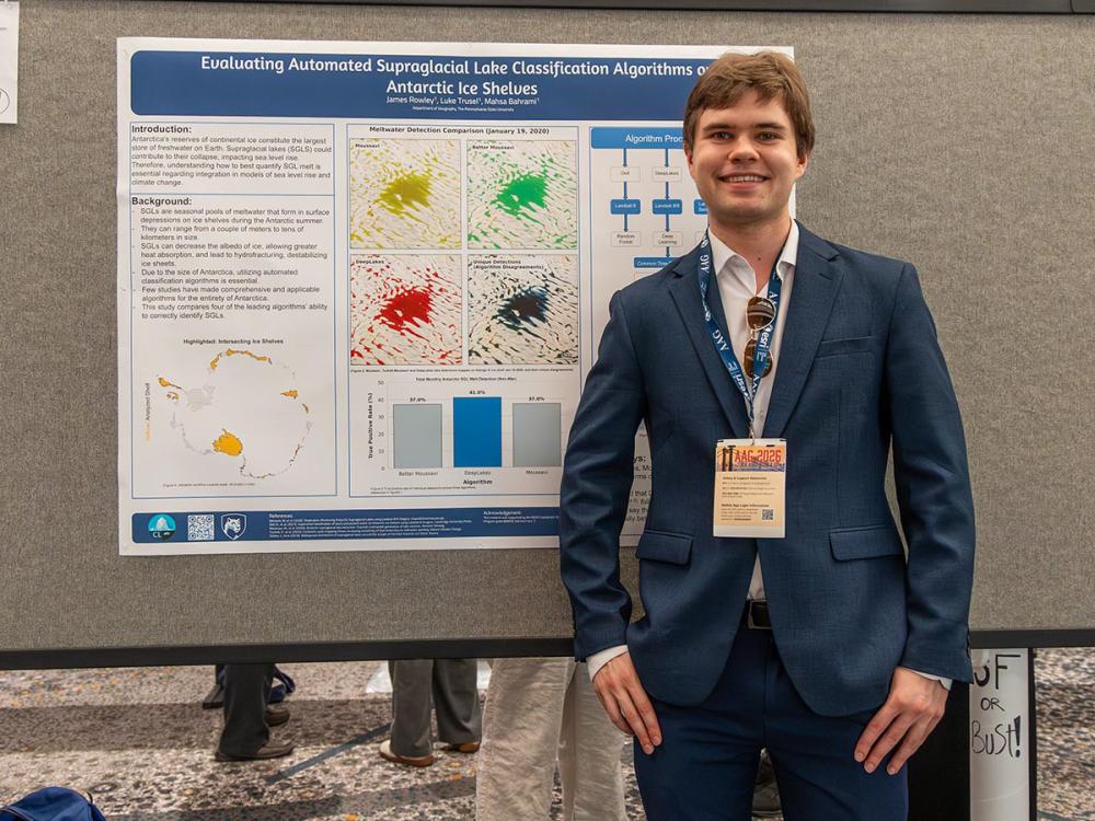 James Rowley wearing a suit stands beside a scientific poster on supraglacial lake classification in Antarctica. He is smiling and looks confident.