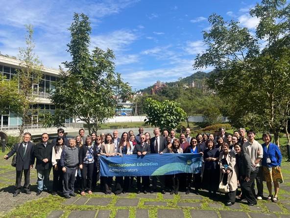 A large group of people holding a banner that says "International Education Administrators"