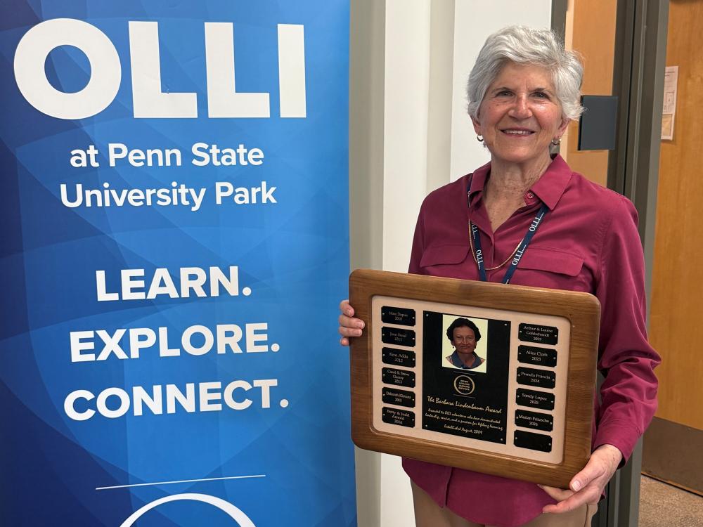Marian Fritzsche stands with an award and an OLLI banner