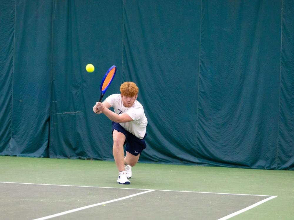 A member of the Penn State Behrend men's tennis team hits a backhand shot.