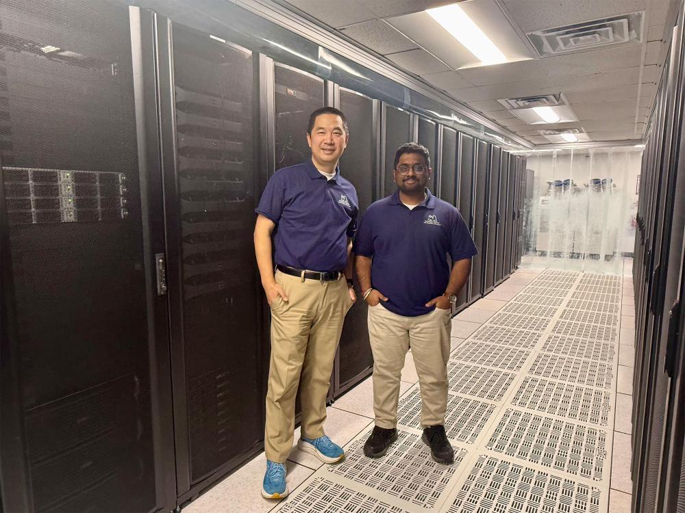 Two researchers at Penn State pose together in front of tall machinery and server racks in a data center