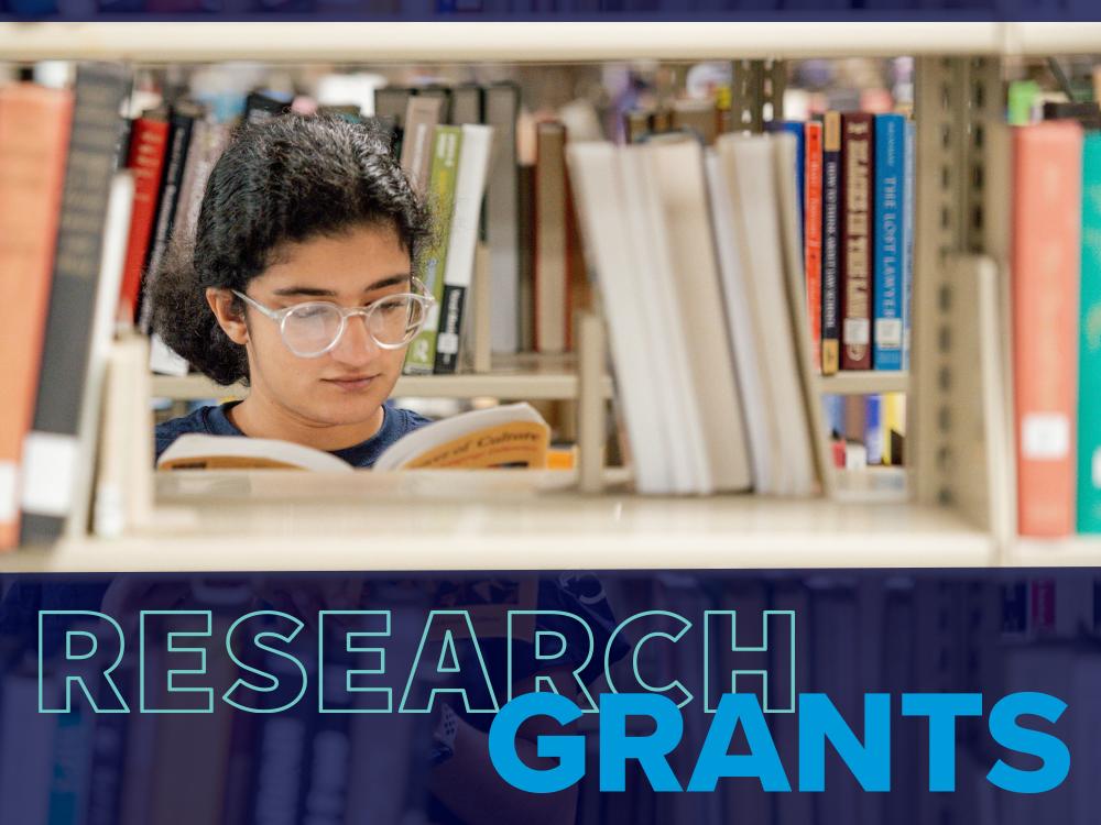 Person wearing glasses and reading a bool behind shelves of books