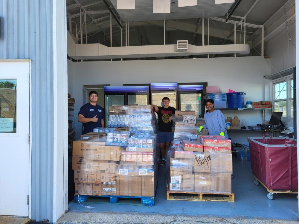 Three student volunteers pose with pallets of food at the Lions Pantry