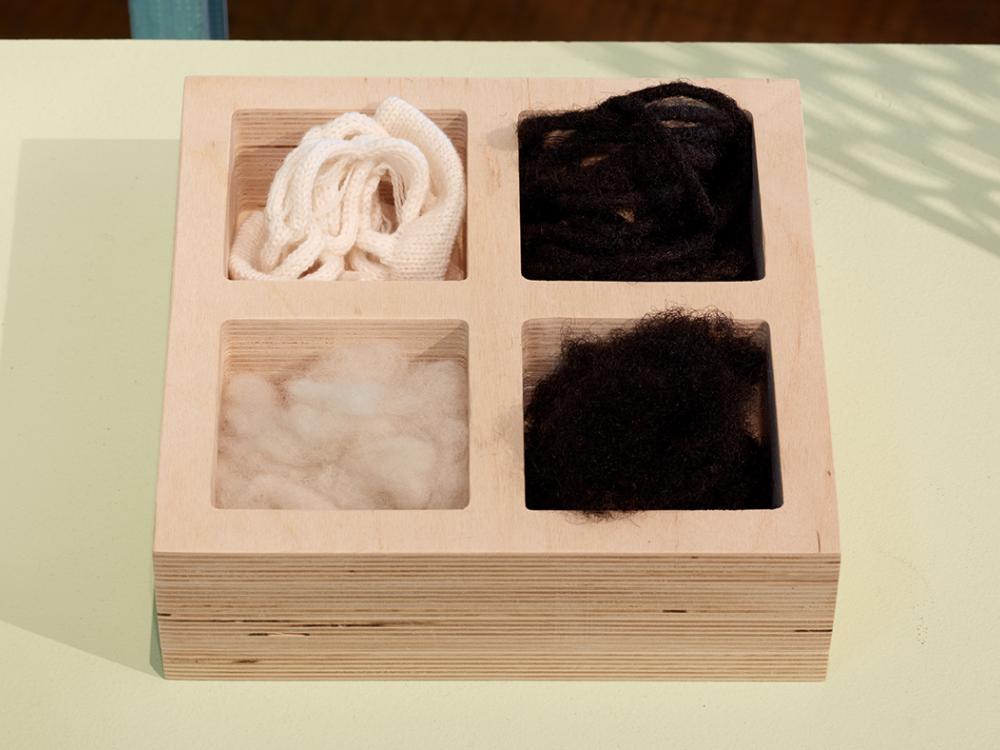 A wooden box with four compartments, the two at left contain wool and the two at right contain Black hair. 