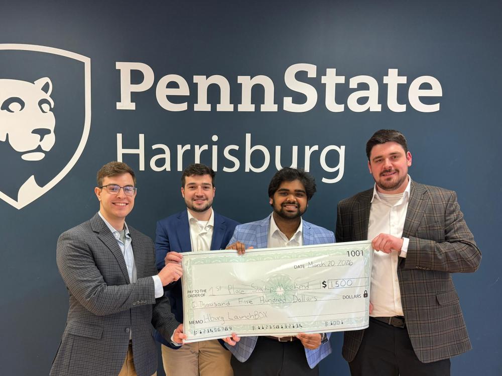 Four students hold up a large check in front of a Penn State Harrisburg sign