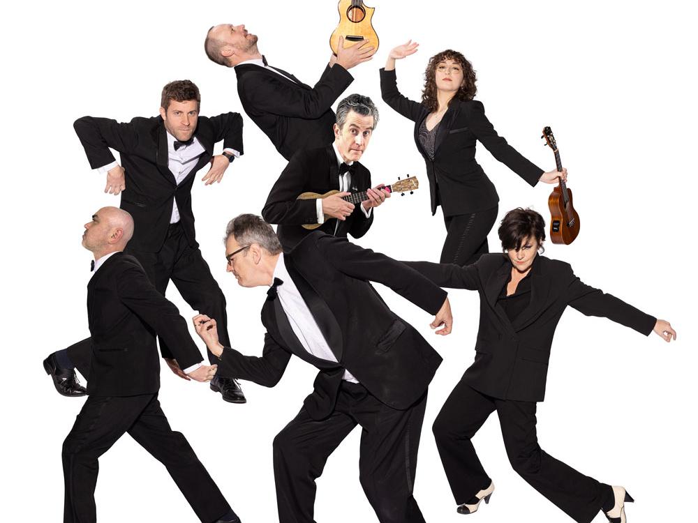 People wearing tuxedos hold ukuleles and make exaggerated poses.