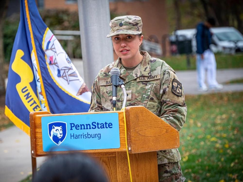 Jessica Barb, wearing a military uniform, speaks from a lectern with the Penn State Harrisburg logo