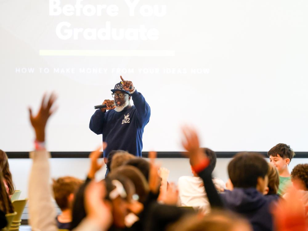 Kevin Sutton with his pointer finger up in the air and students raising their hands