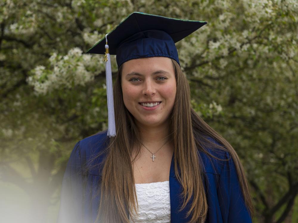 Penn State female graduate smiles for a photo wearing blue commencement reglia. 