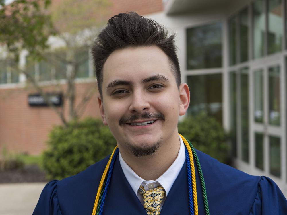 Penn State graduate smiles for a photo wearing blue commencement reglia. 