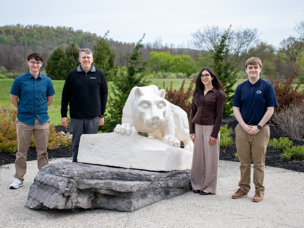 3 students and a male representative from global tech company, Broadcom, smile in front of the lion shrine outside.