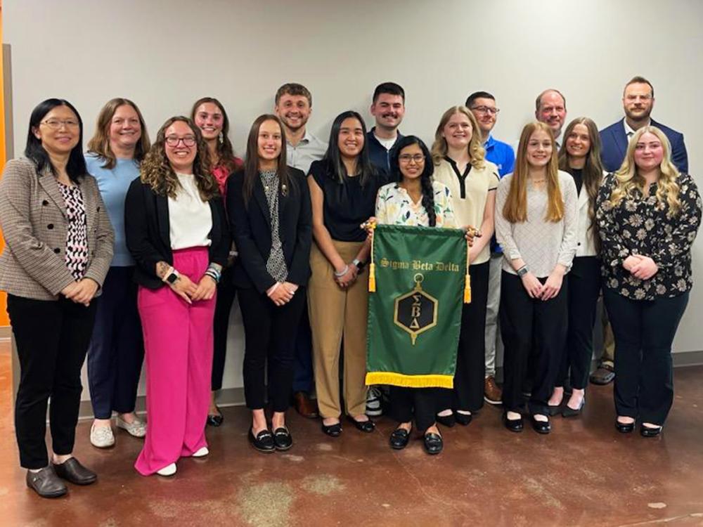 Group of students and faculty pose with a Sigma Beta Delta banner during an honor society induction ceremony