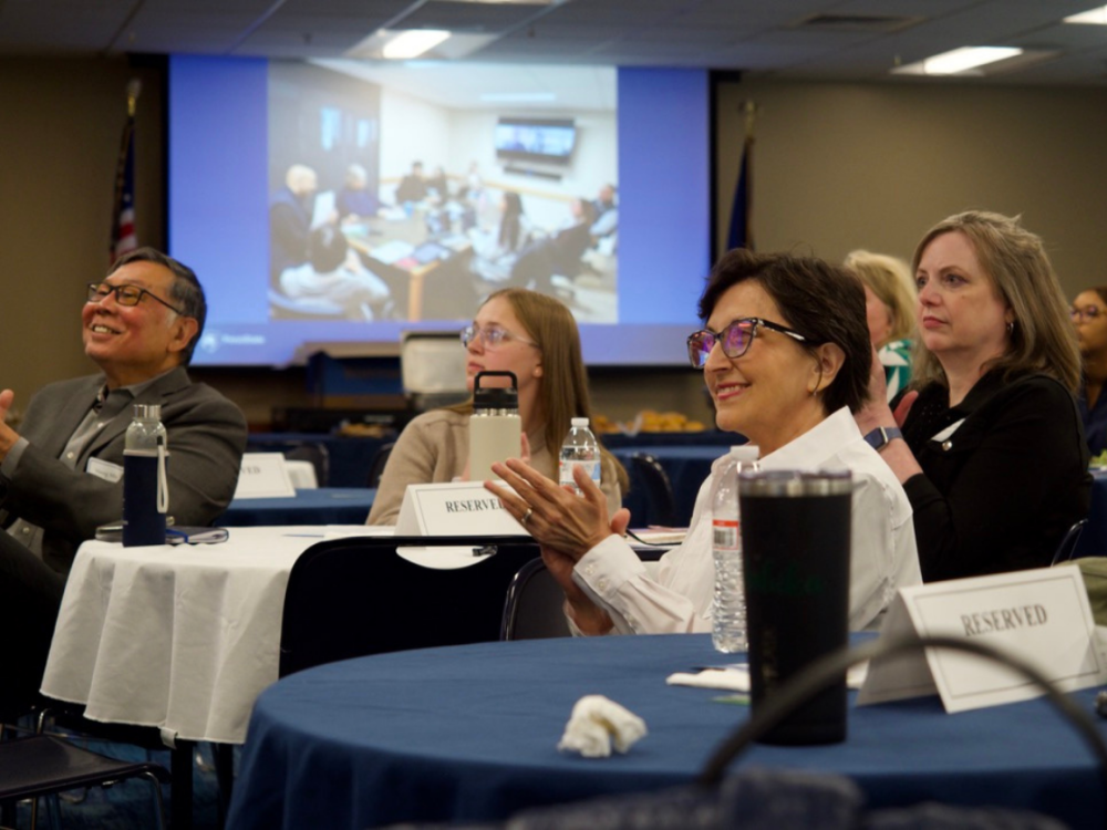 faculty and students sit at round tables smiling and clapping
