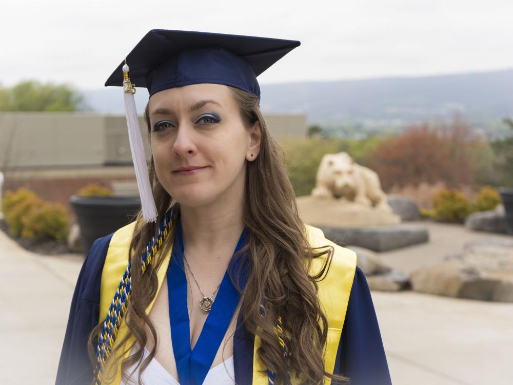 Penn State female graduate smiles for a photo wearing blue commencement reglia. 