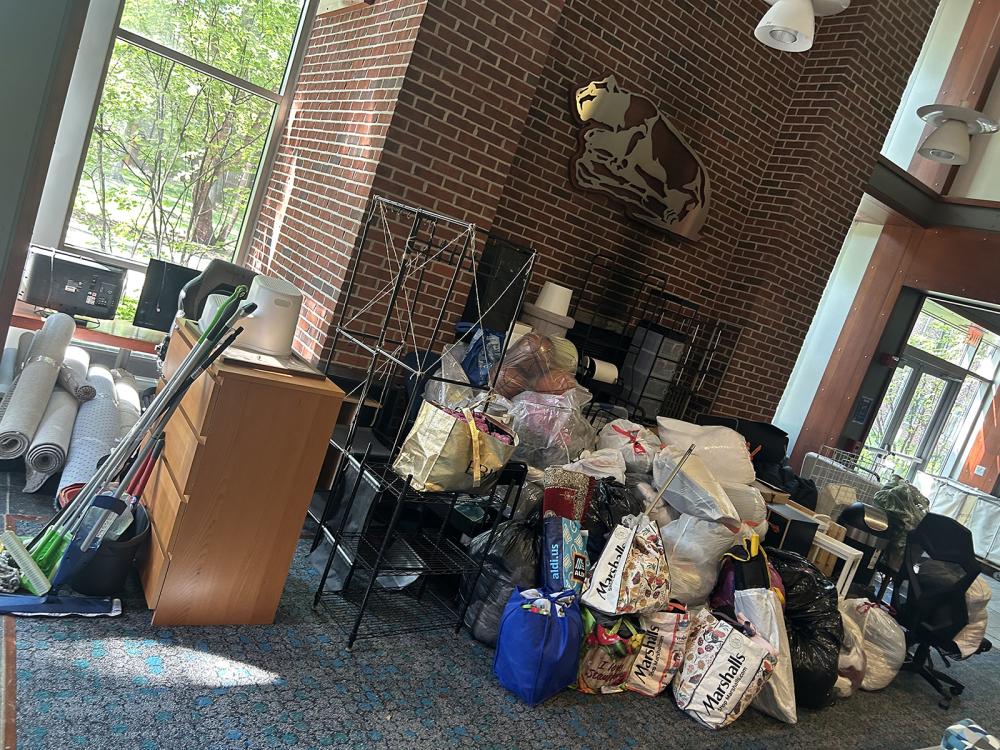 Rolled rea rugs, bedding, brooms, and more donations wait in the Ivy Lounge for pickup