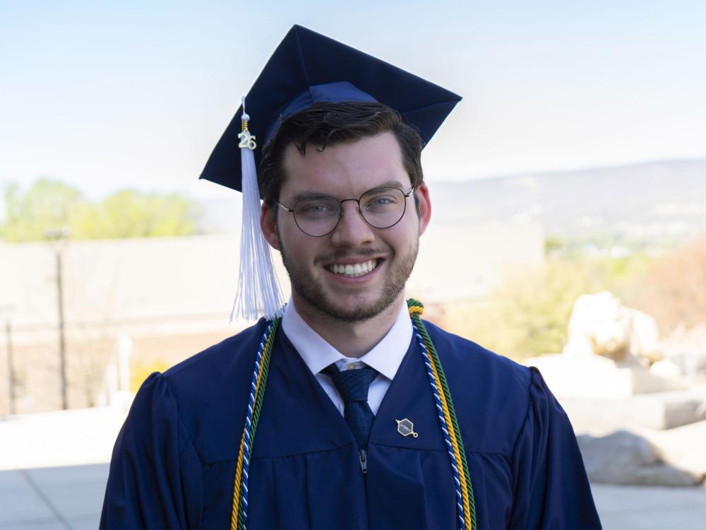 Penn State male graduate smiles for a photo wearing blue commencement reglia. 